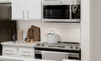 Virtually staged kitchen with stainless appliances, white quartz countertops, white subway tile, white shaker cabinets, pot on stove and cutting boards with spices